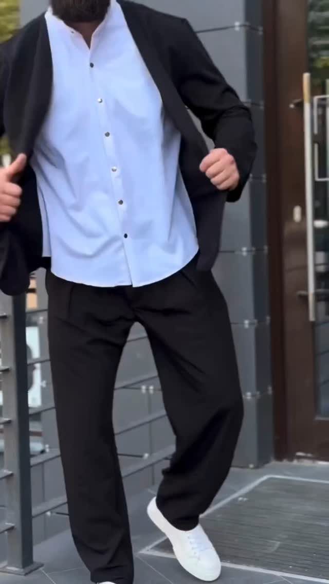 A man dressed in a black blazer, white shirt, black trousers, and white sneakers.