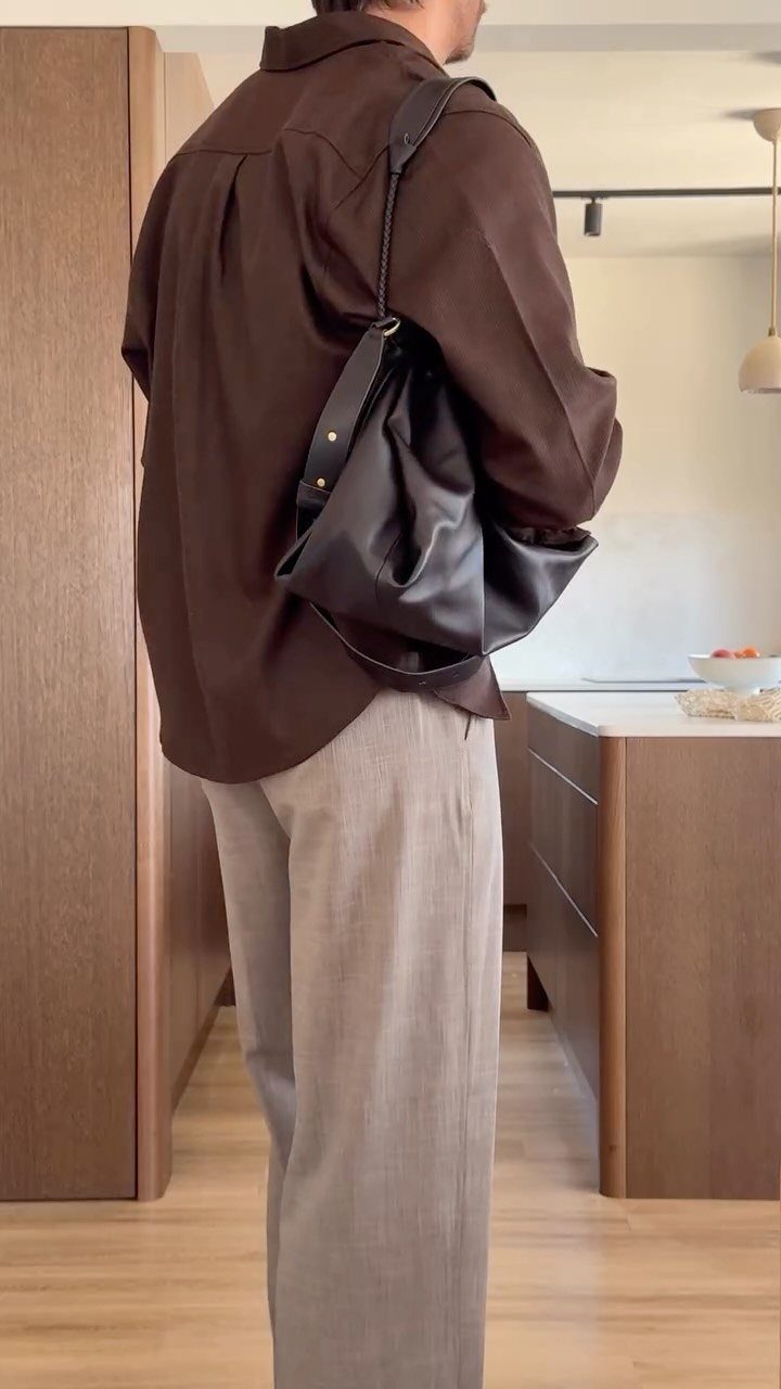 Person wearing a dark brown long-sleeved shirt and grey trousers carrying a black leather bag.