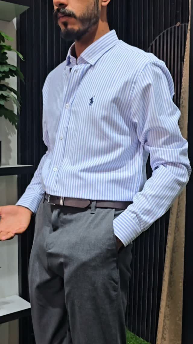 Man wearing a blue striped button-down shirt with grey trousers and a brown belt.