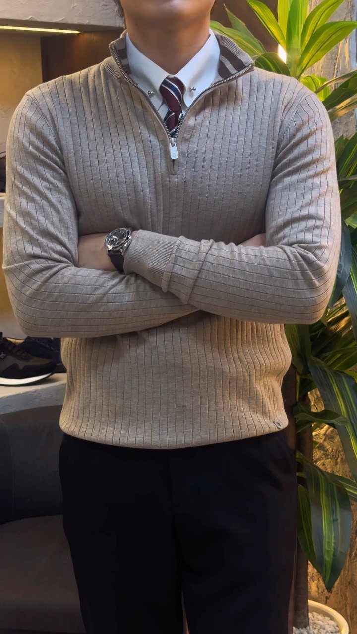 Man wearing a beige ribbed quarter-zip sweater over a white shirt and striped tie.