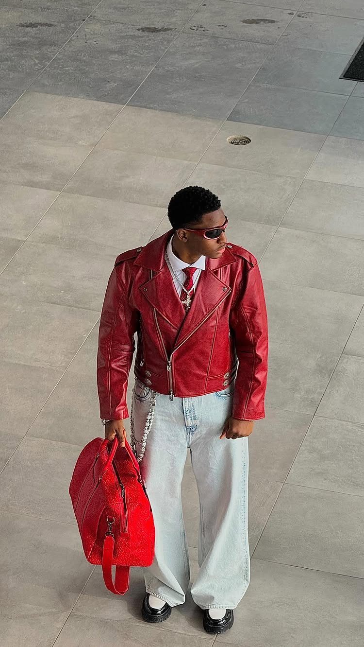 A person wearing a red leather jacket, light blue jeans, and carrying a red bag.