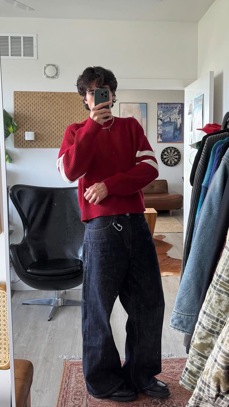 A person wearing a red sweater and dark wide-leg jeans posing for a mirror selfie.