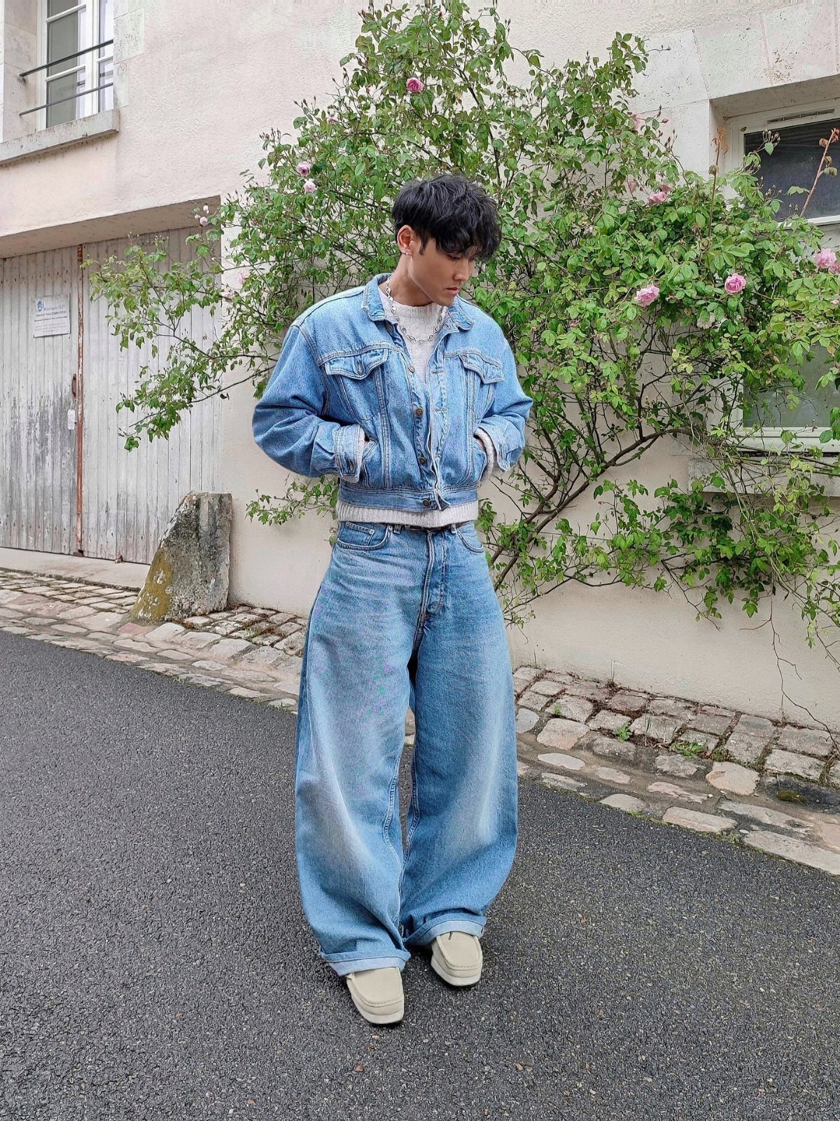 A young man posing in a denim jacket and oversized wide leg jeans on a street.