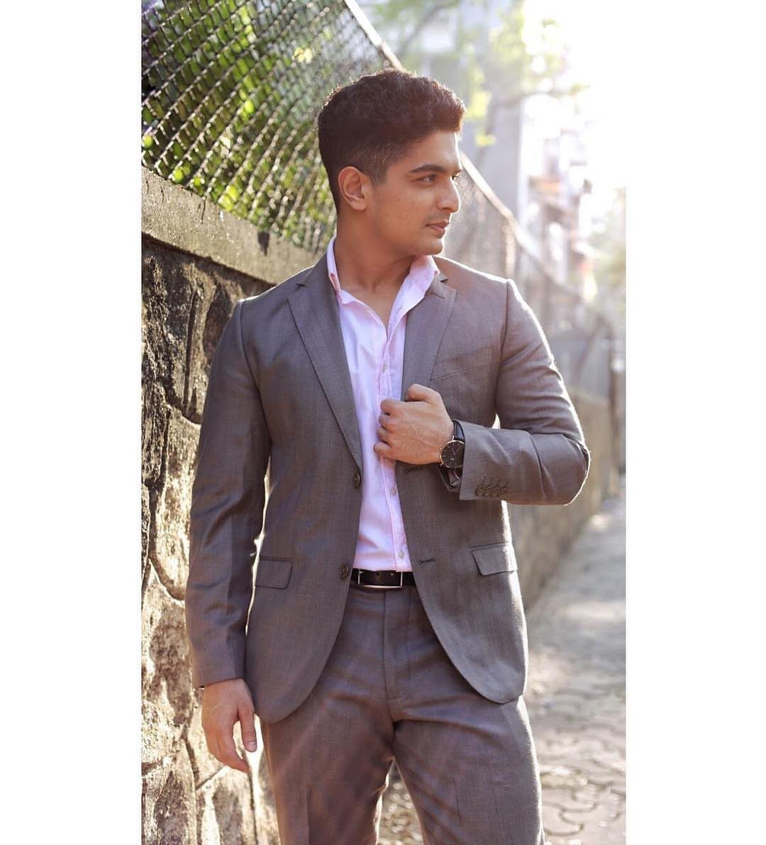 A man wearing a pink shirt, grey suit jacket, and matching grey trousers standing outdoors.