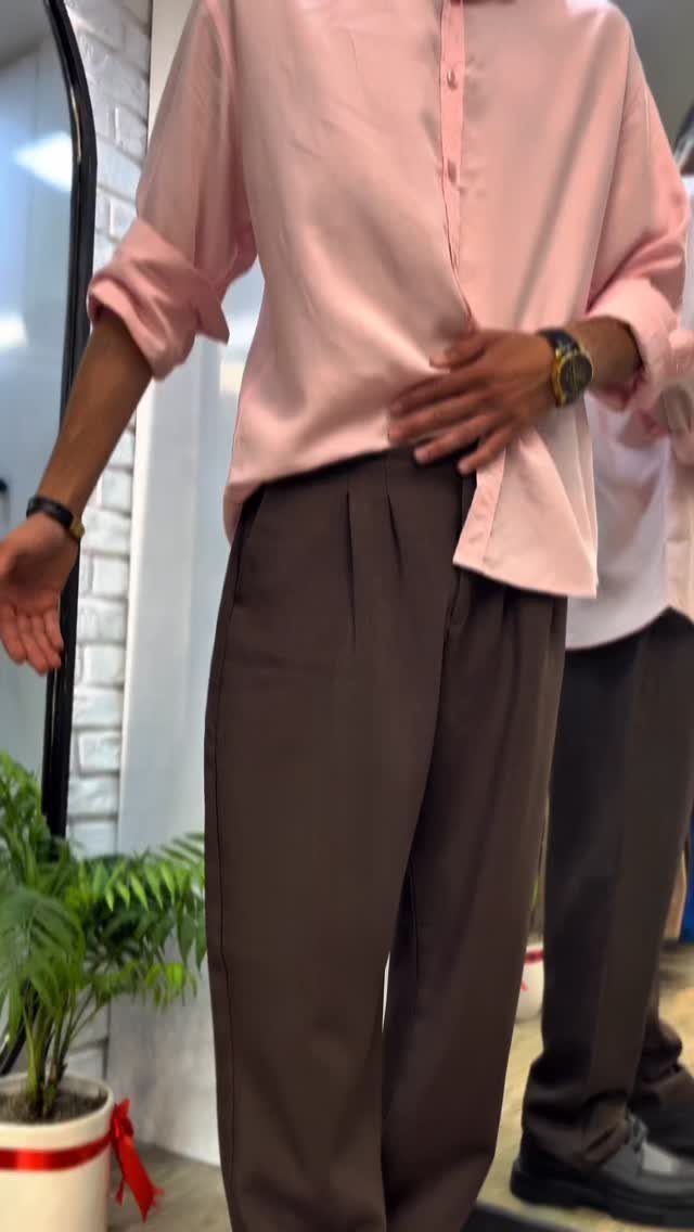 Man wearing a pink button-down shirt paired with dark brown pleated trousers.