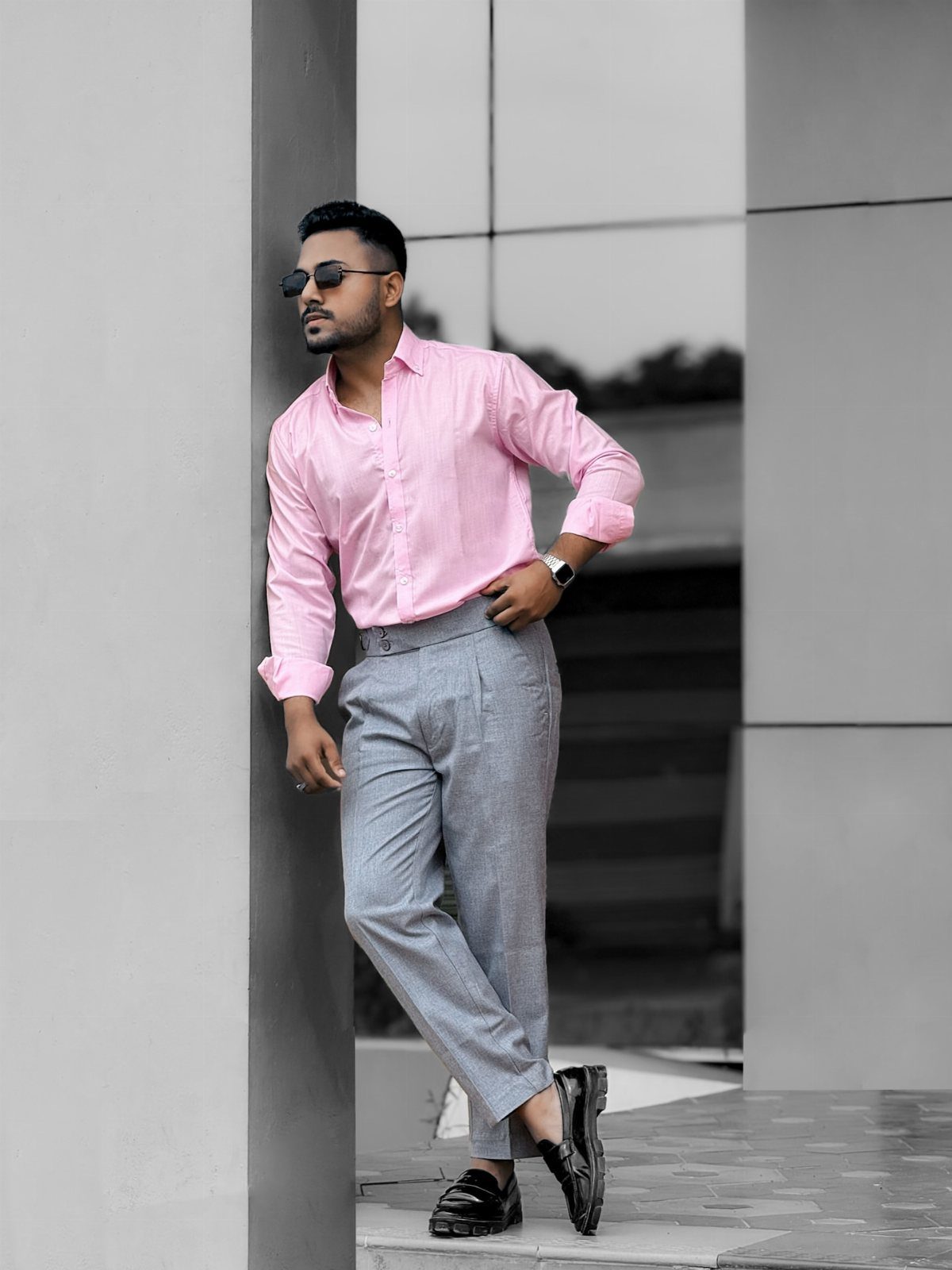 Man in a pink shirt and grey trousers leaning against a pillar.