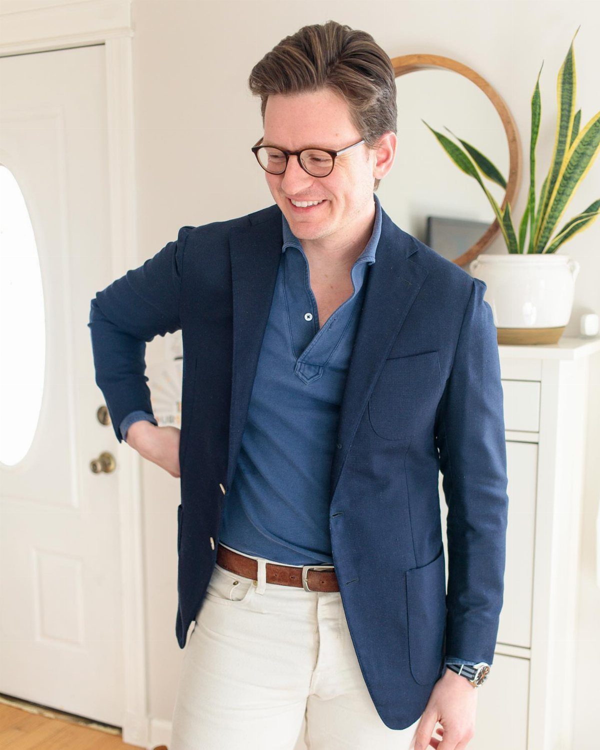 A man in a navy blazer and blue long sleeve polo shirt smiling indoors.