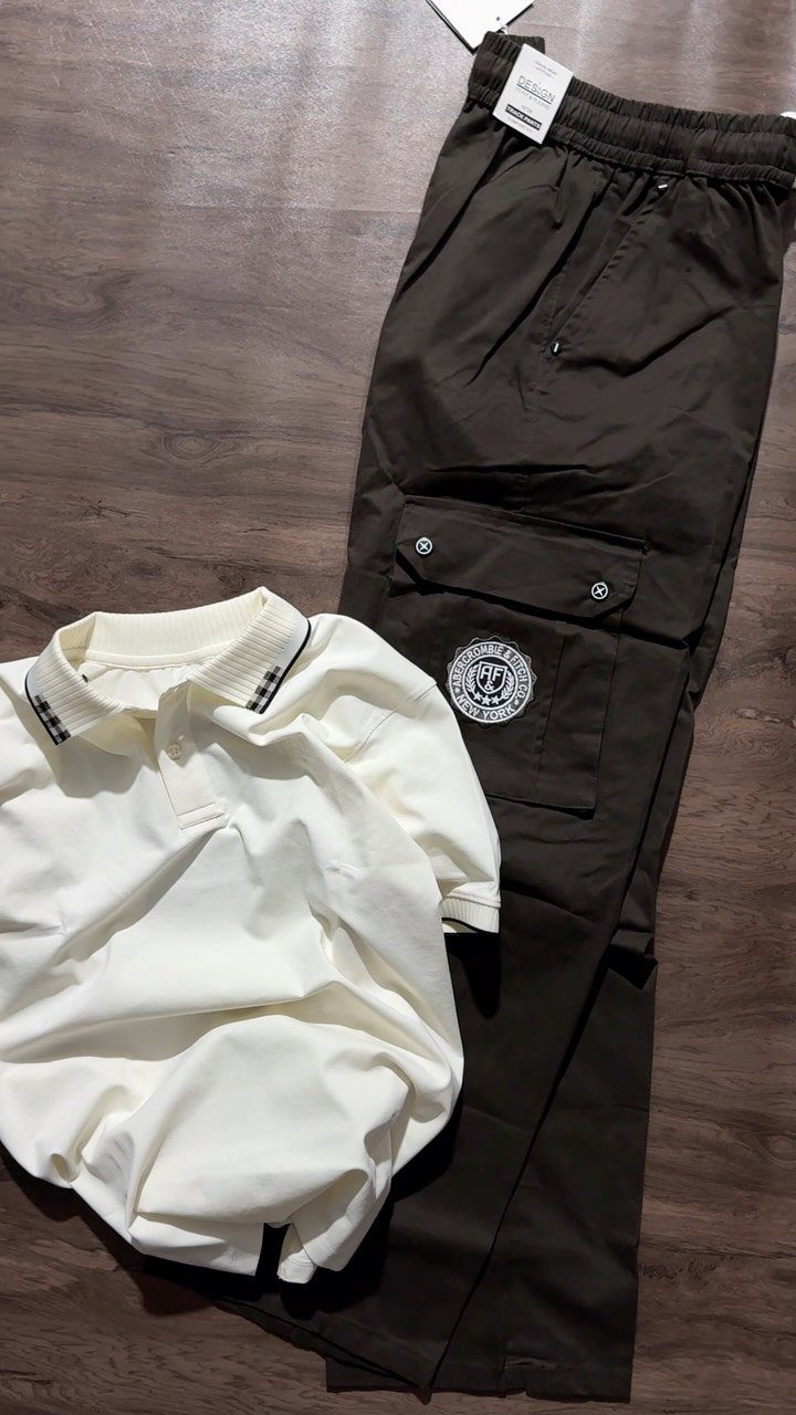 White polo shirt and dark brown cargo pants laid flat on a wooden floor.