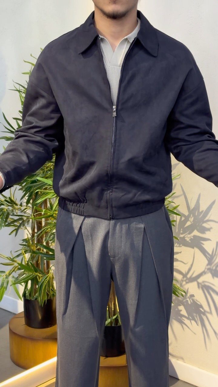 Man wearing a navy zip-up jacket over a grey polo shirt and grey trousers.