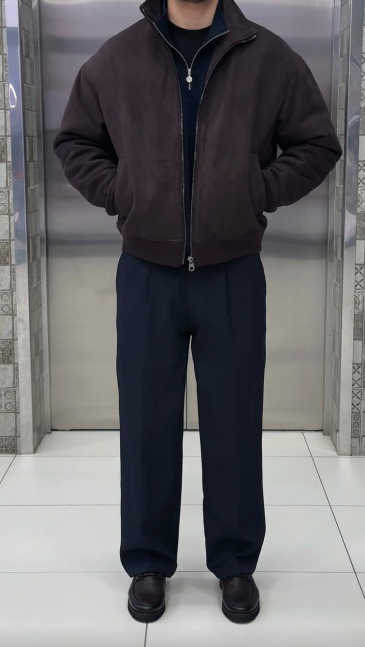 A person wearing a brown jacket over a navy quarter-zip sweater and navy trousers.