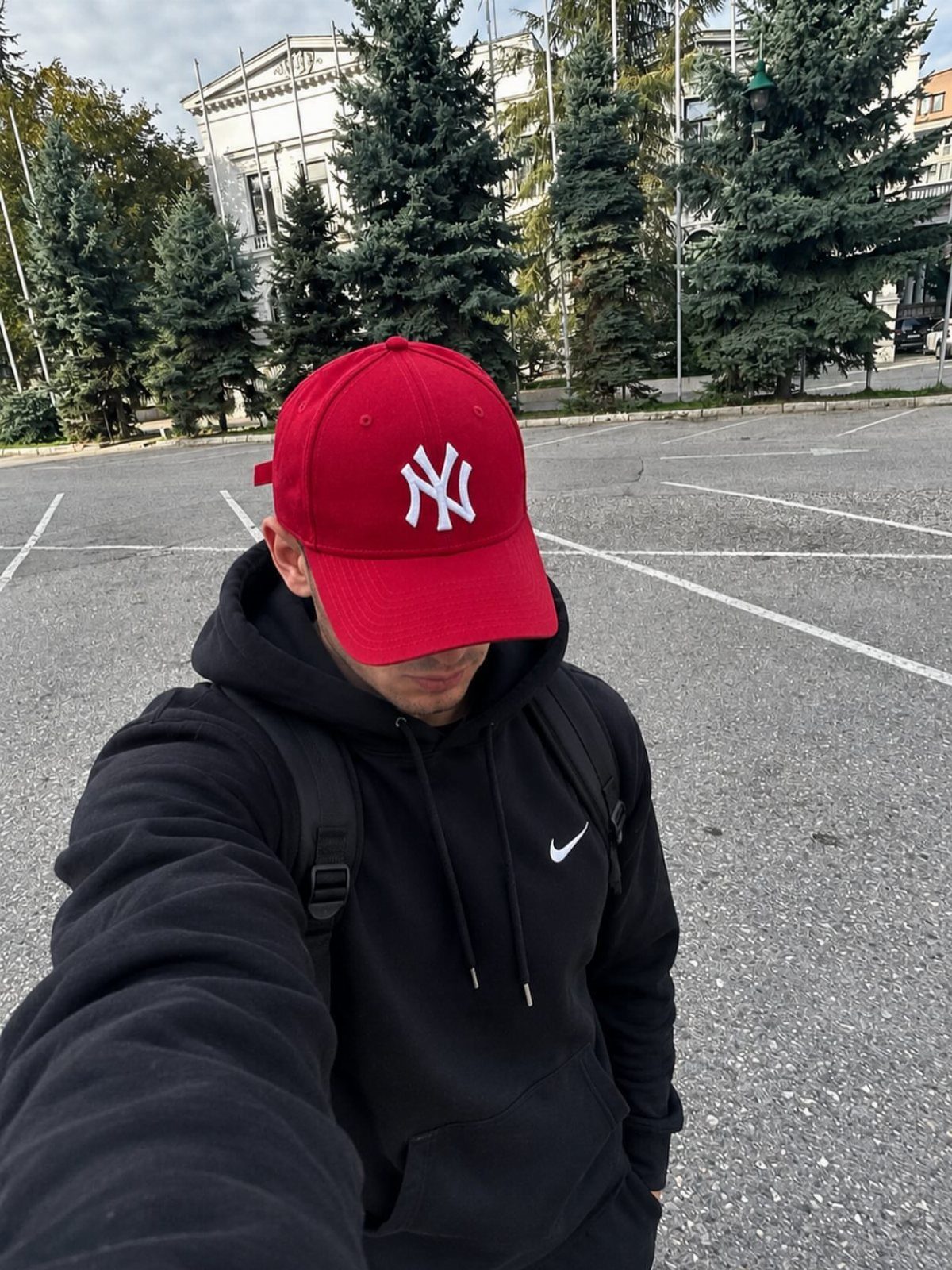 Man in a red baseball cap and black Nike hoodie standing in a parking lot.