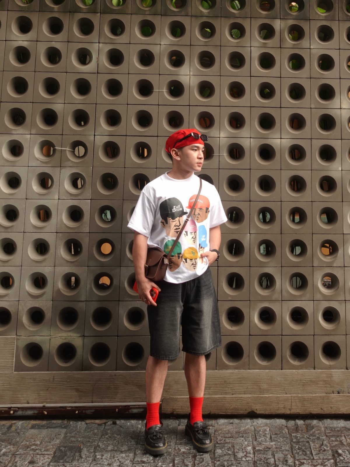 A young man wearing a red cap, white graphic t-shirt, black shorts, and red socks.