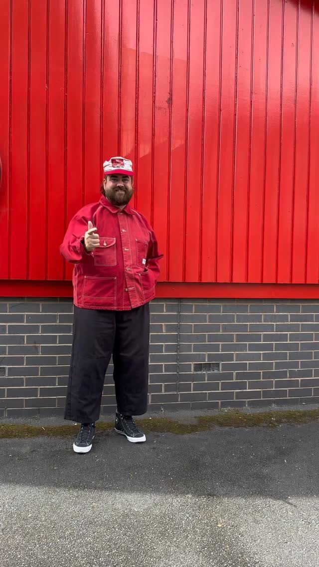 A man wearing a red hat, red jacket, and black pants standing against a red wall.