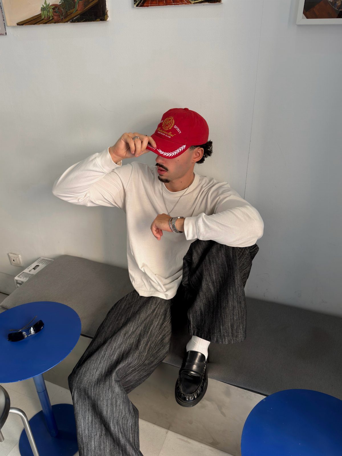 Man in a white long-sleeved shirt and red baseball cap sitting on a bench.