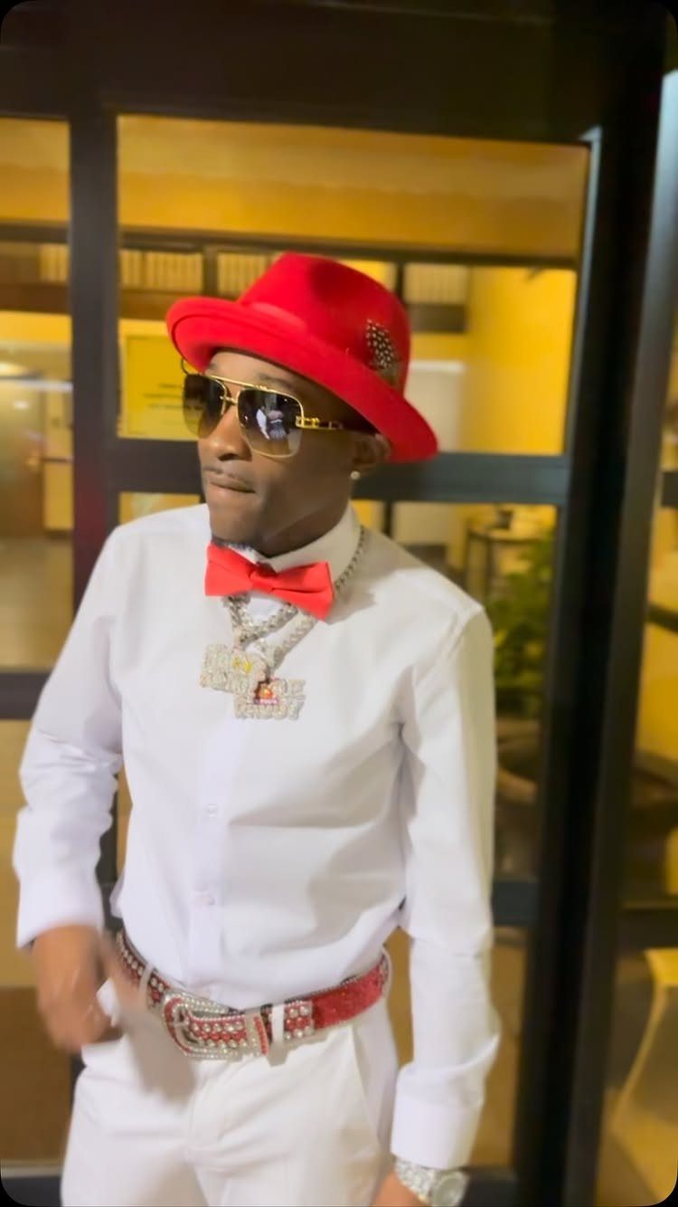 Man in white shirt, red bowtie, and a bright red fedora hat wearing sunglasses.