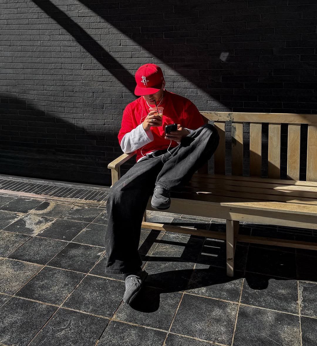 Man in a red hat and red shirt sitting on a wooden bench outdoors.