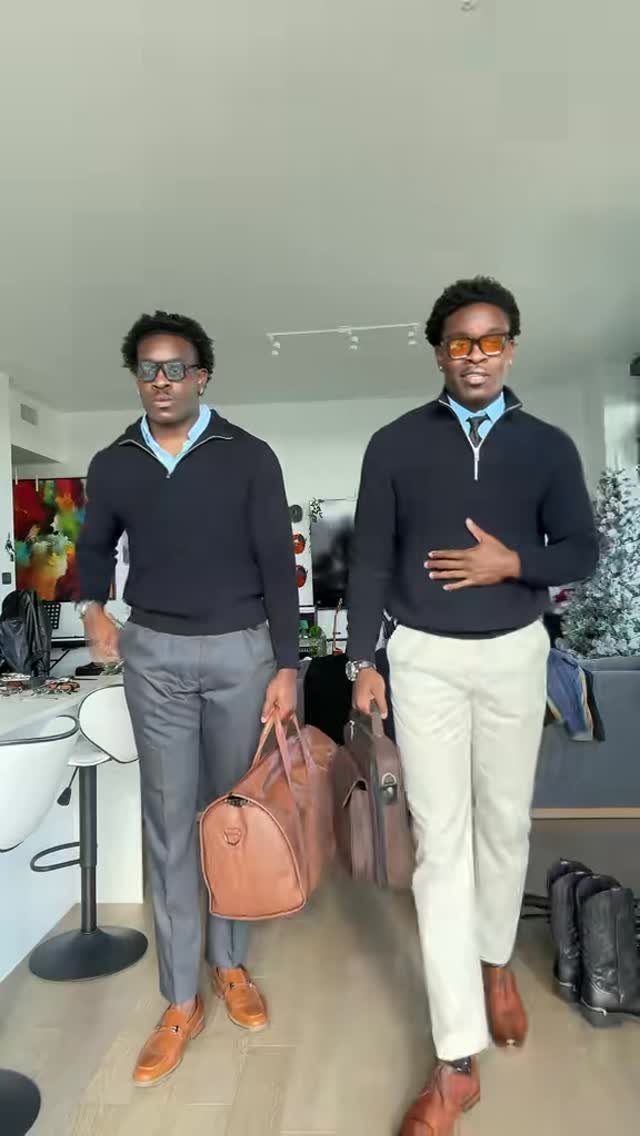 Two men posing in smart-casual spring outfits while carrying leather travel bags indoors.