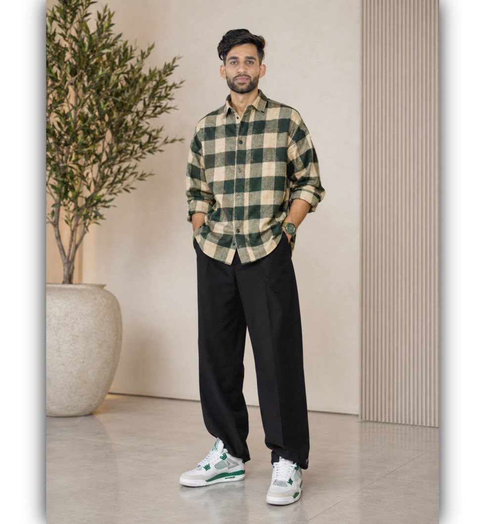 Man wearing a green and beige checkered flannel shirt with black trousers and white sneakers.