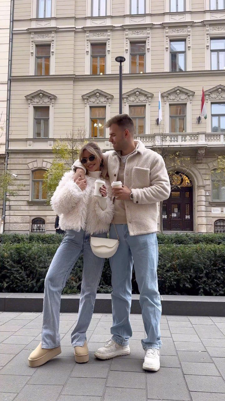 A man in a cream fleece jacket and light blue jeans standing with a woman outdoors.