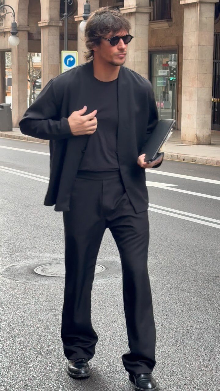 Man in an all-black outfit with an unstructured blazer and trousers standing on a city street.