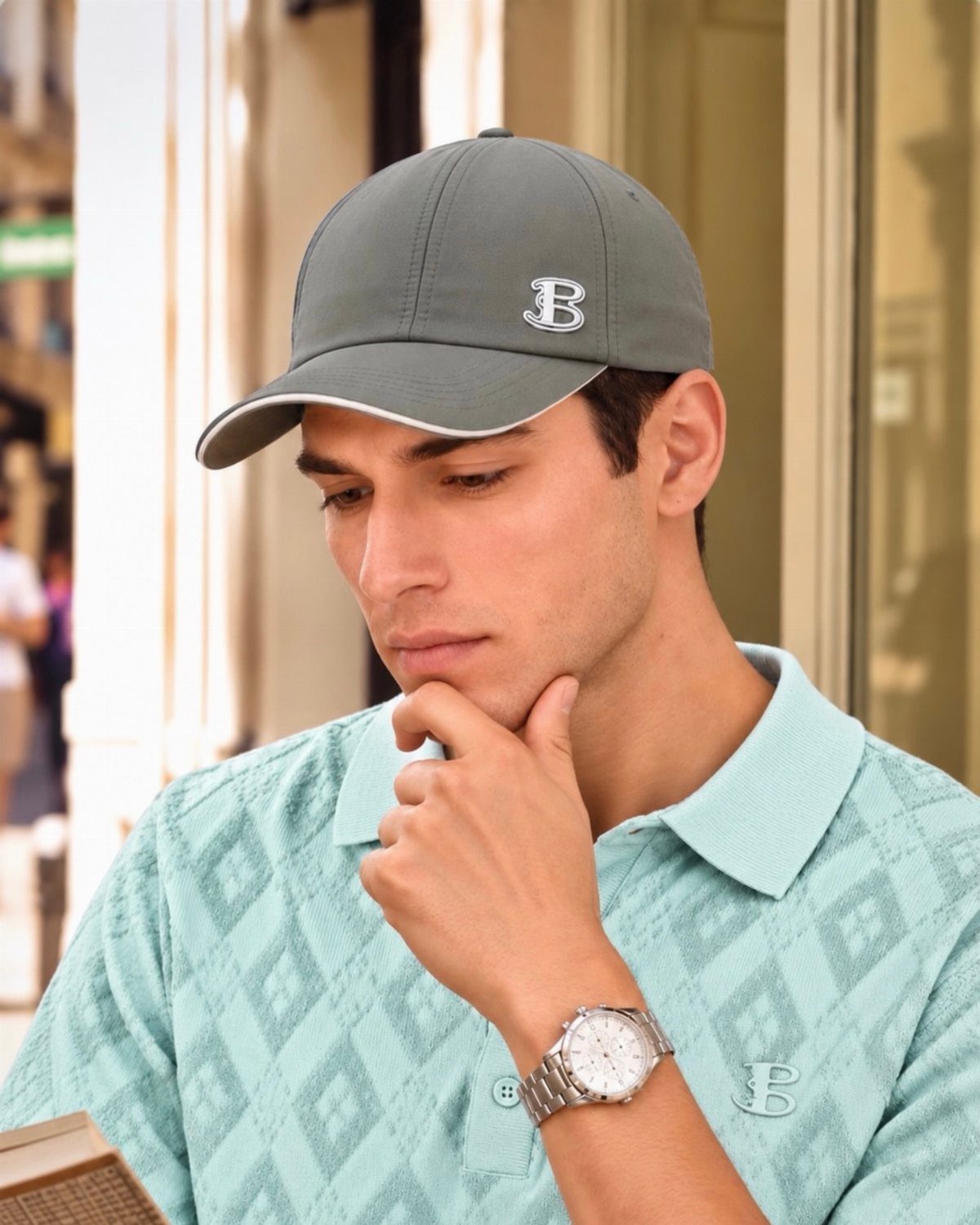 Young man wearing a light turquoise patterned polo shirt and a grey baseball cap.