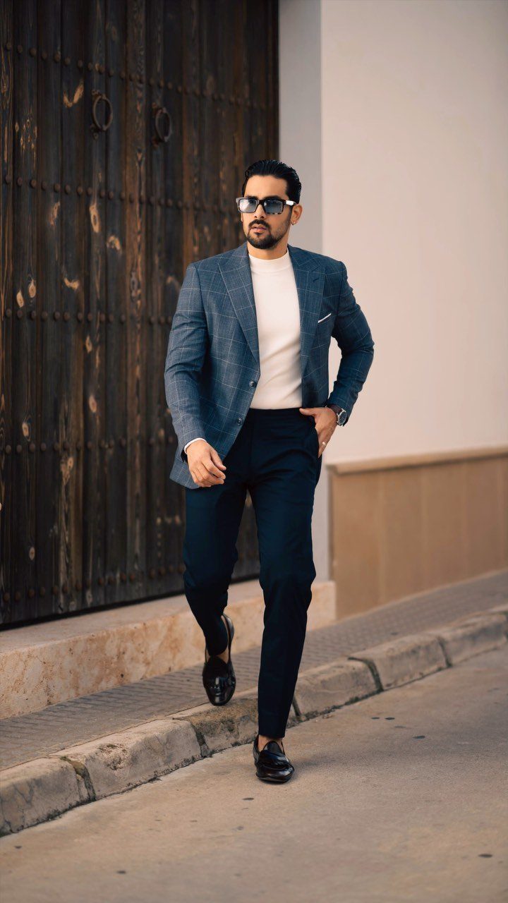 Man walking in a blue blazer, white sweater, navy trousers, and black loafers.