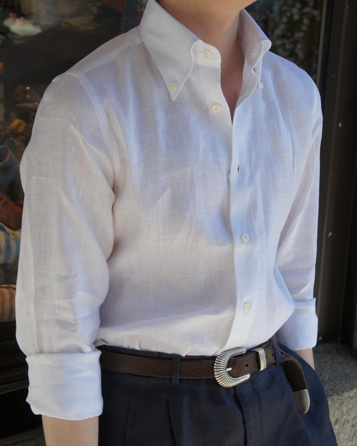 A person wearing a crisp white linen button-down shirt and dark navy trousers with a brown belt.