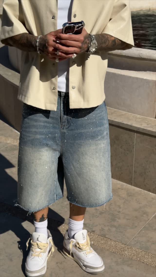 Person wearing cream shirt, speckled denim shorts, white socks, and white sneakers standing outdoors.