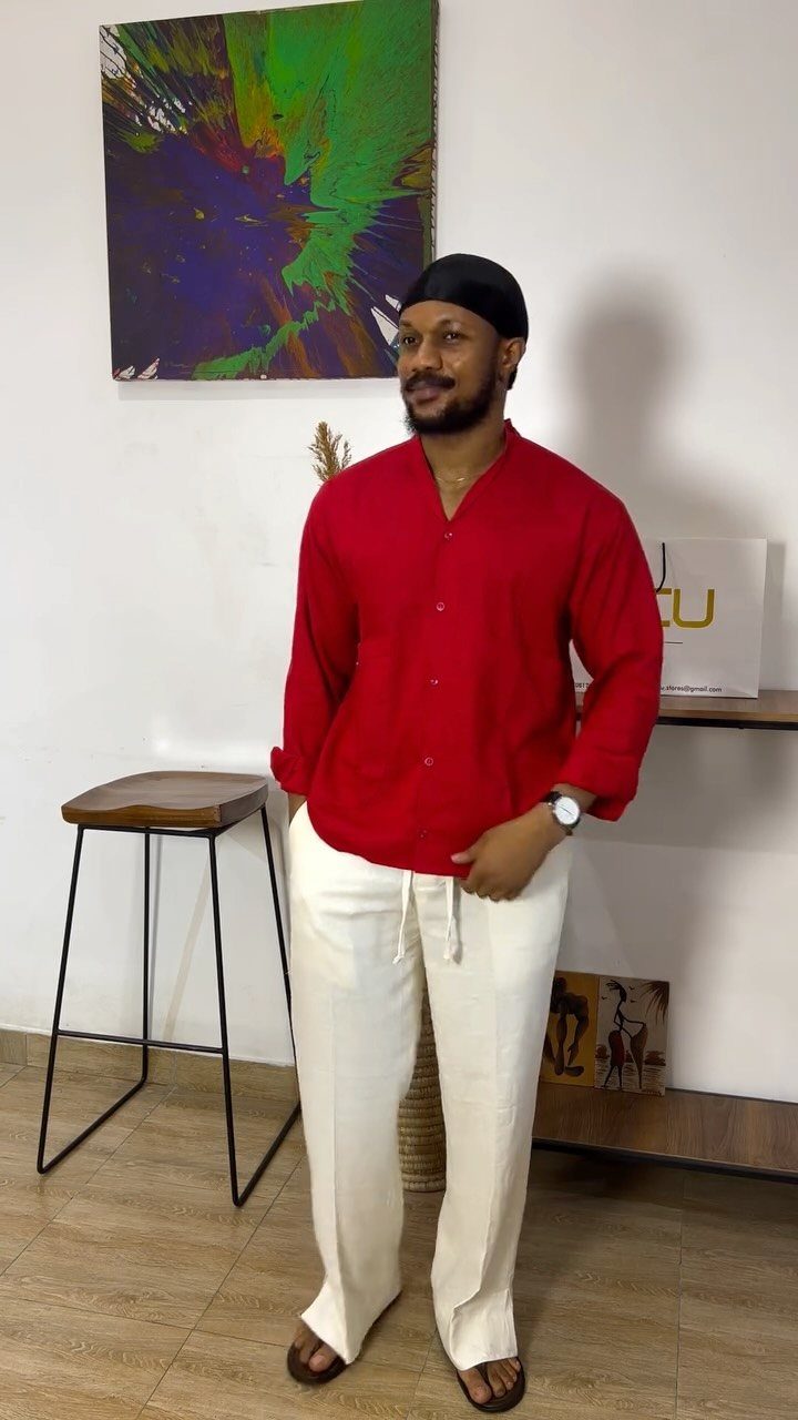 Man in a red linen shirt and cream linen trousers standing in a room.