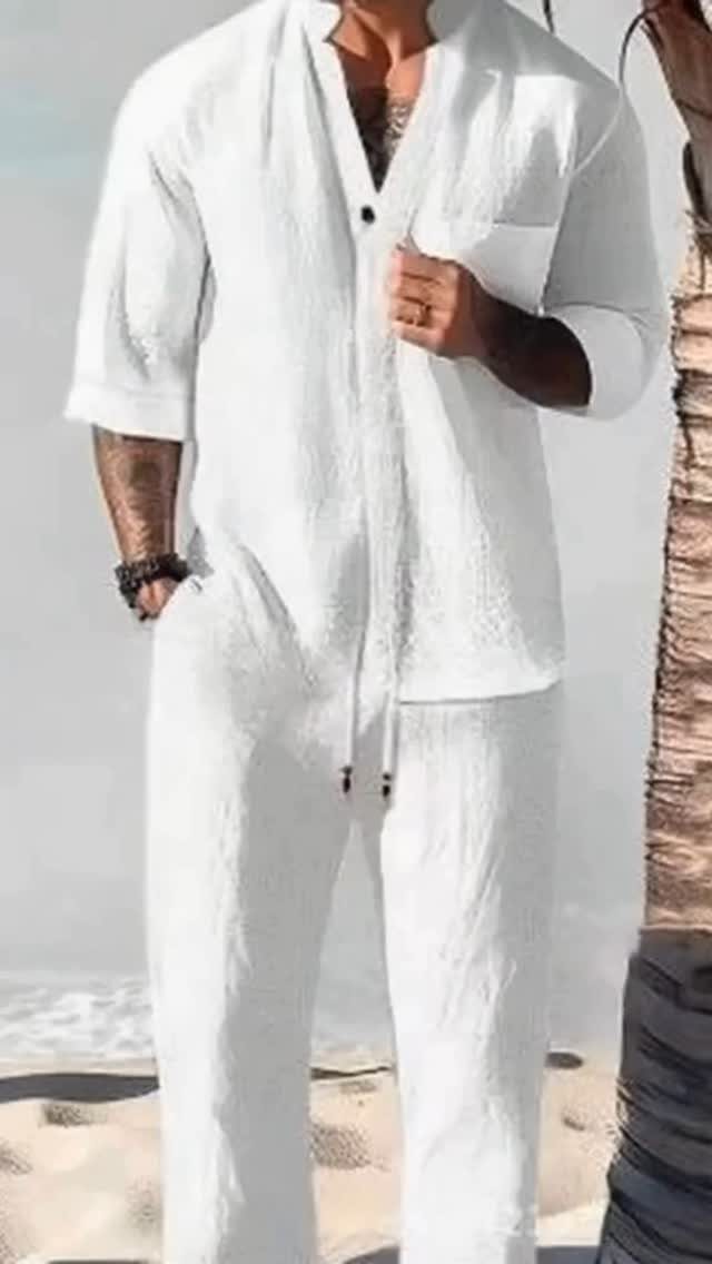 A man wearing a white linen shirt and matching linen trousers standing on a sunny beach.