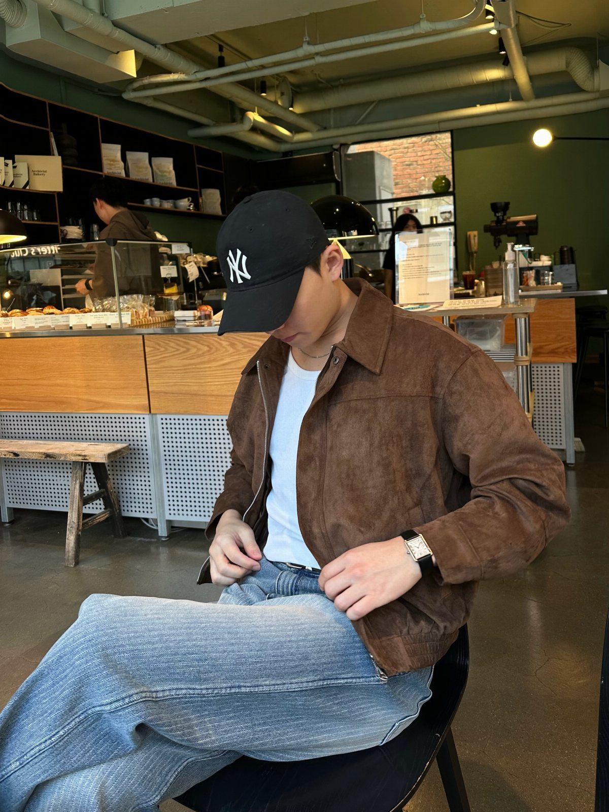 A person in a brown suede jacket and white t-shirt sitting in a cafe.