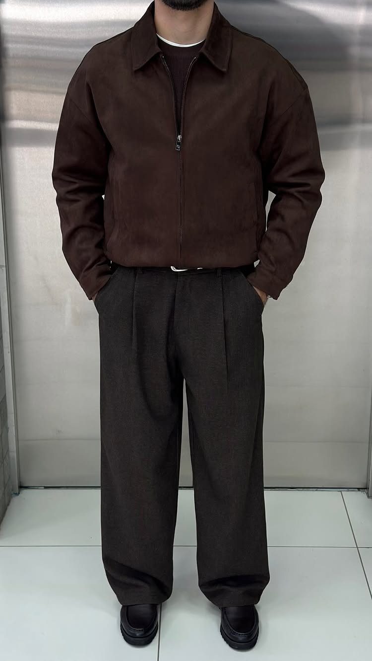 A person wearing a brown suede jacket and dark wide-leg trousers with a white belt.