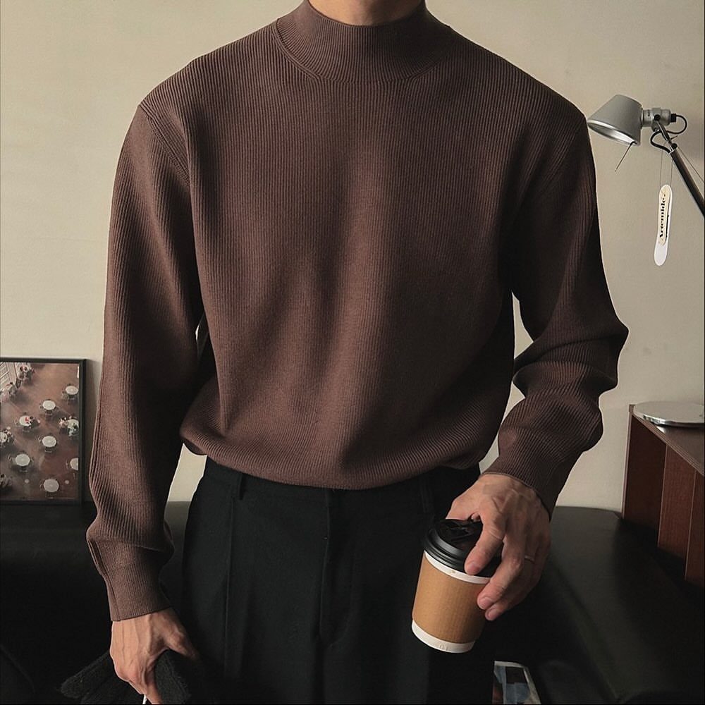 Man wearing a brown ribbed turtleneck sweater paired with black trousers while holding a coffee cup.
