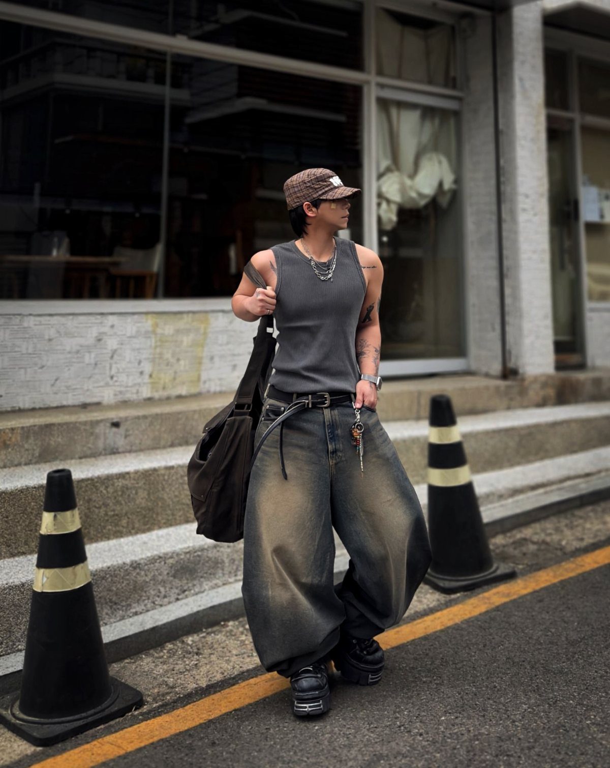 A person walking in a grey tank top and oversized blue jeans on a city street.