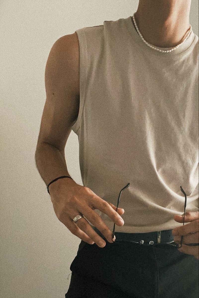 Person wearing a beige tank top tucked into black trousers with a belt.