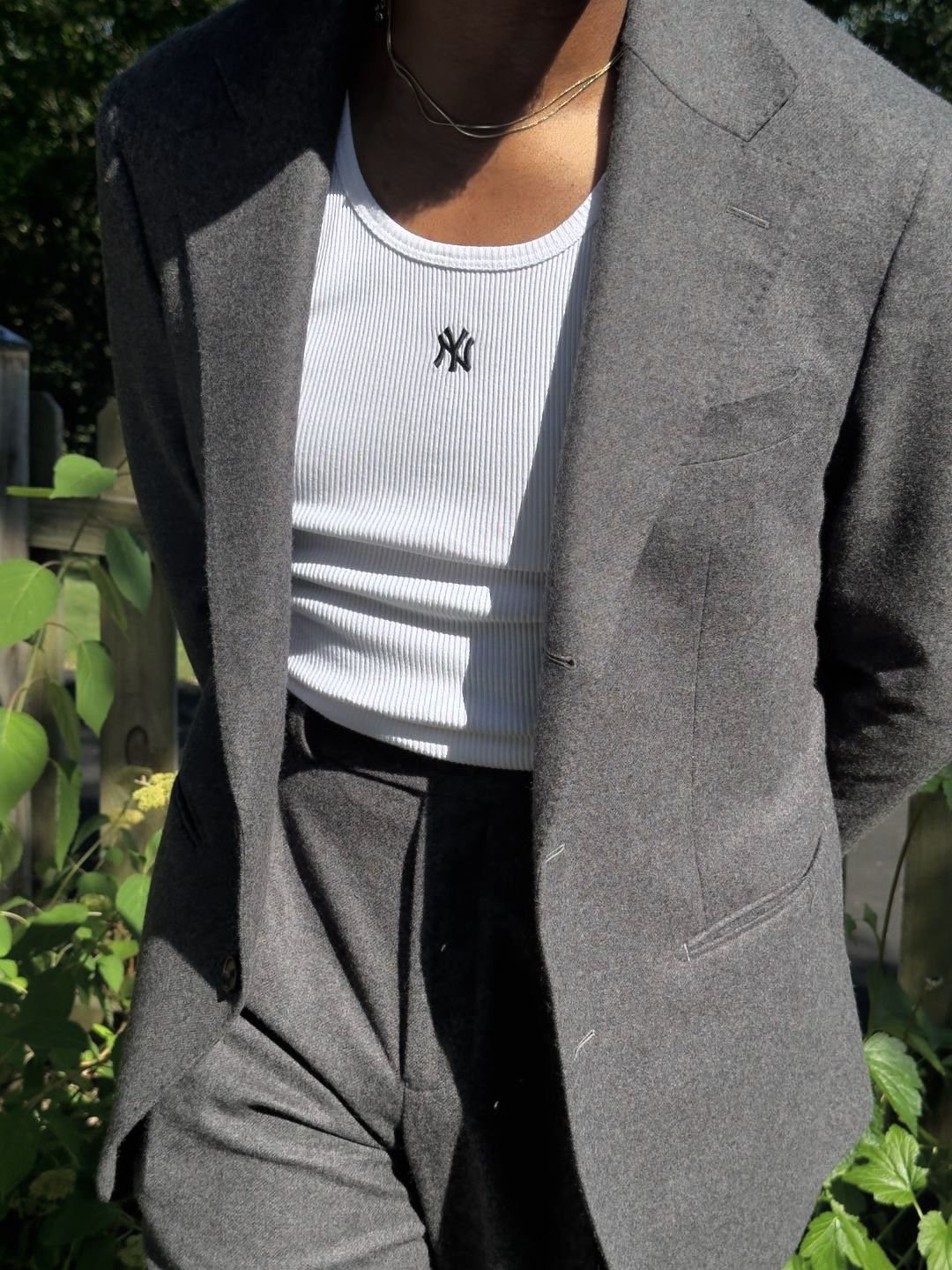 Person wearing a white ribbed tank top under a grey blazer and matching trousers.