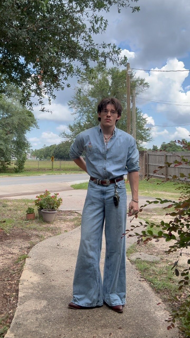 A man posing in a denim shirt and wide-leg bell-bottom jeans on a sidewalk.