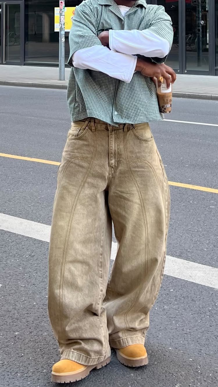 A person wearing oversized green checkered shirt and baggy tan trousers on a city street.