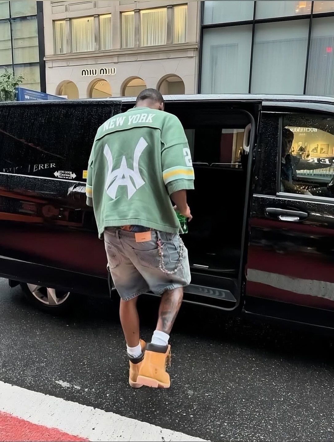 Man in green jersey and denim shorts wearing tan Timberland boots stepping out of a van.