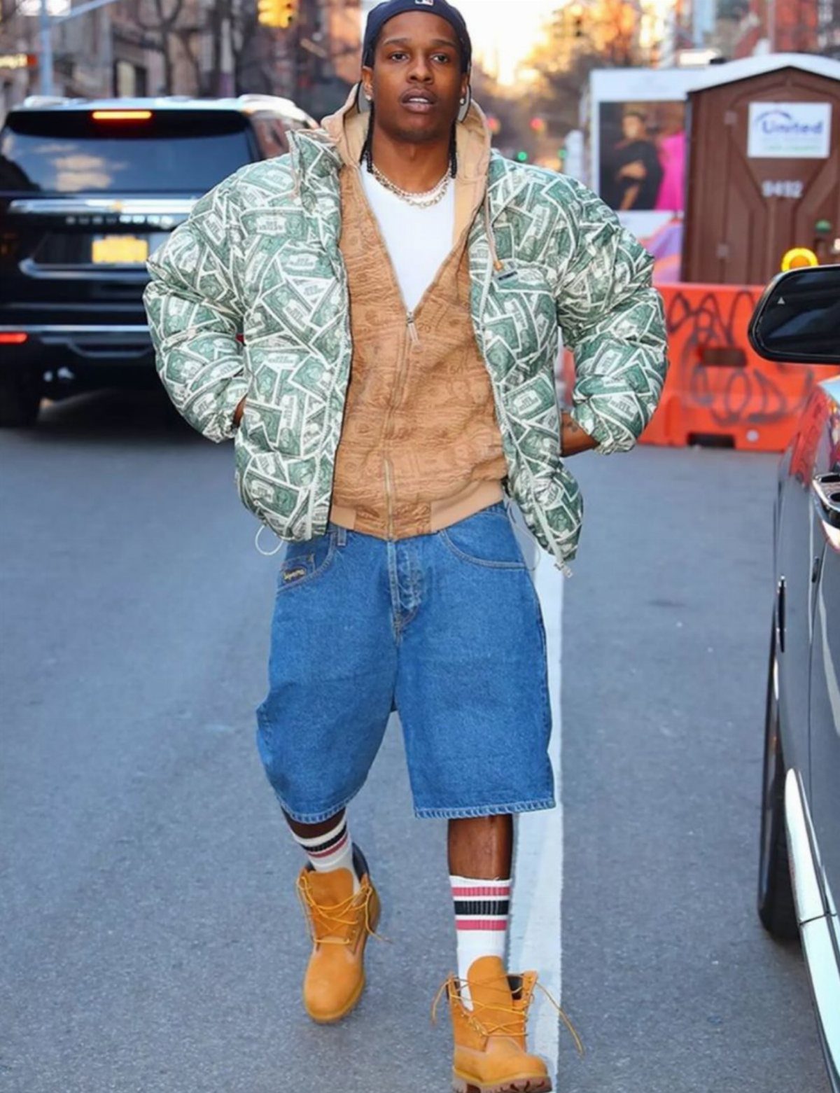 Man walking in a city wearing a patterned puffer jacket, denim shorts, and tan Timberland boots.