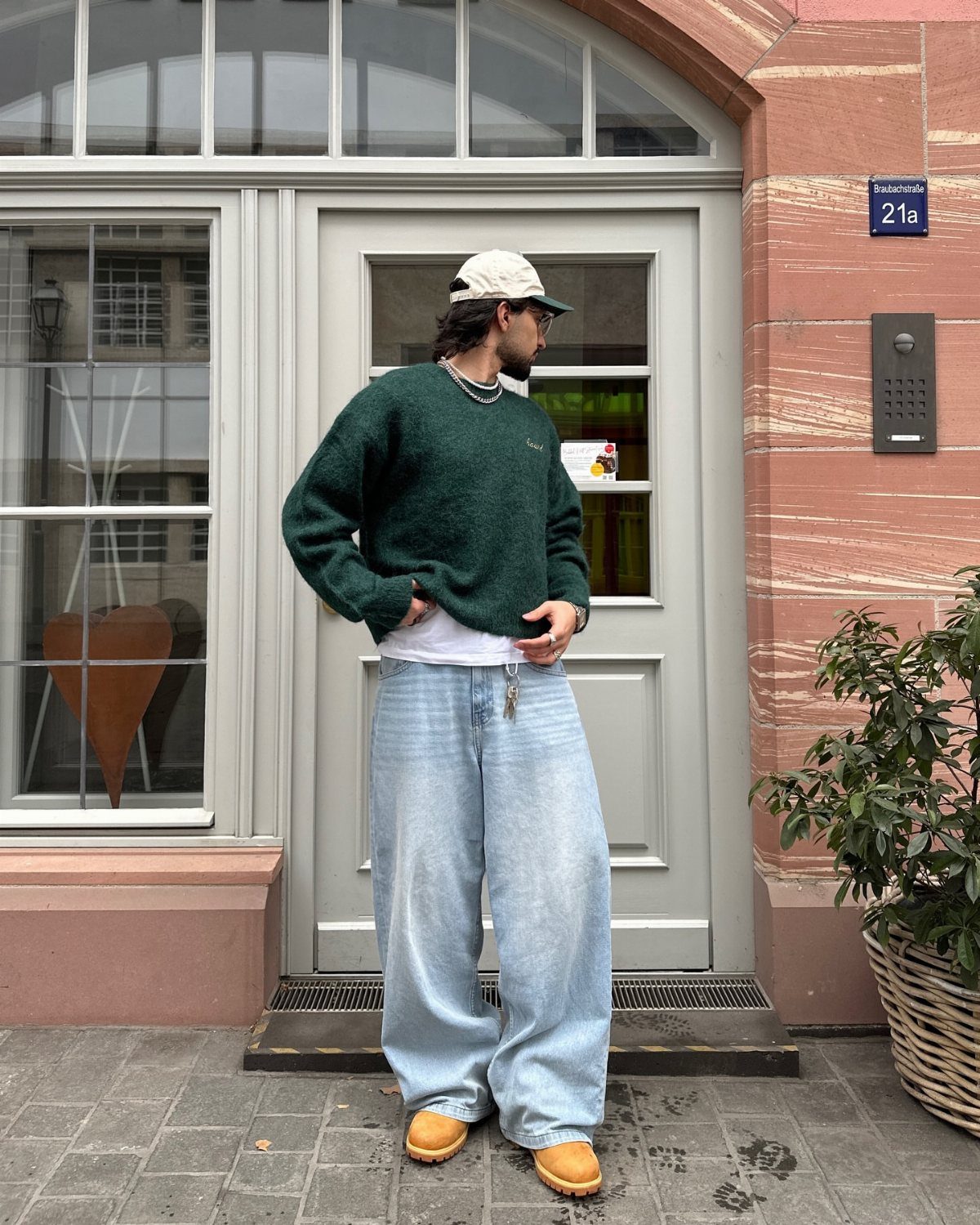 A person wearing a green sweater, wide light blue jeans, and tan Timberland boots standing outdoors.