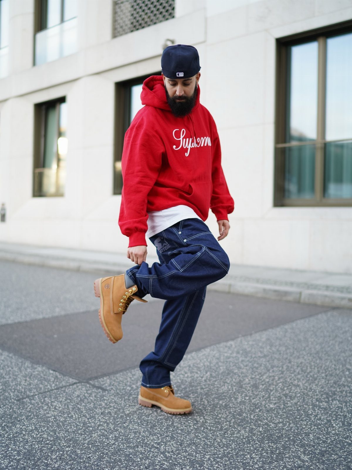 Man in a red hoodie and dark denim pants wearing tan Timberland boots outdoors.