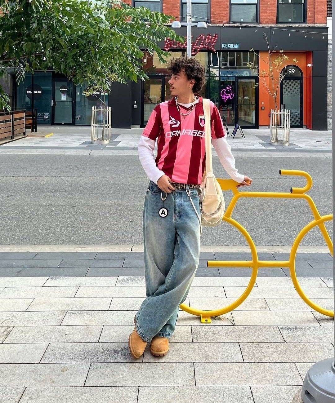 A man wearing a striped jersey, baggy jeans, and tan Timberland boots standing outdoors.