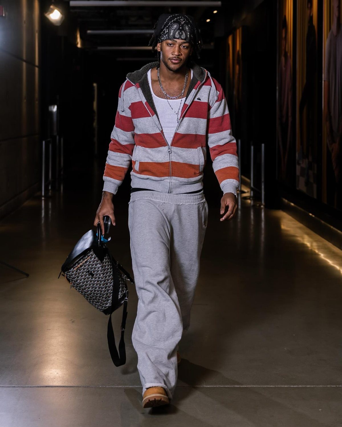 Man walking in a hallway wearing a striped hoodie, grey sweatpants, and tan Timberland boots.