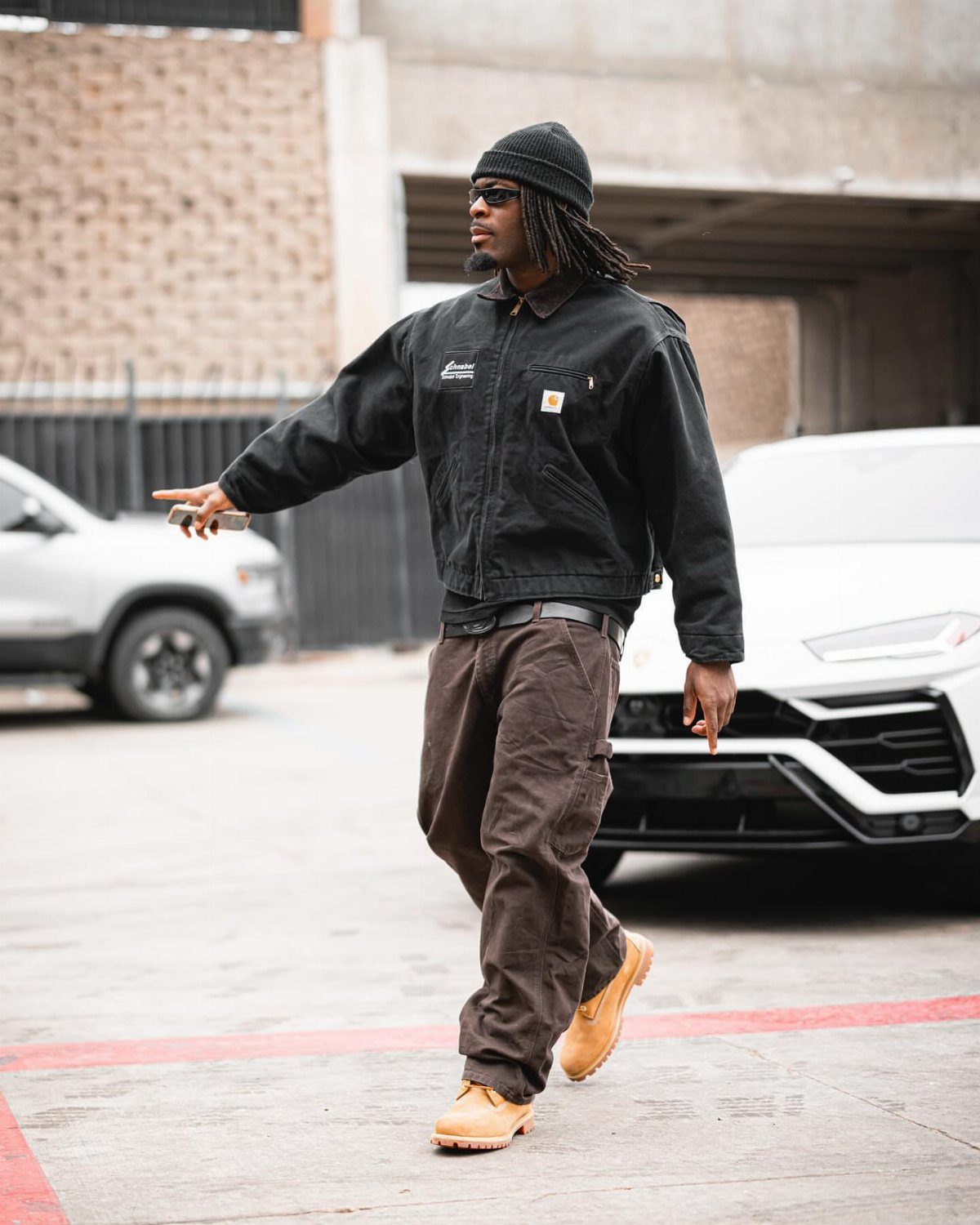 A man walking in a black jacket, brown pants, and tan Timberland boots.
