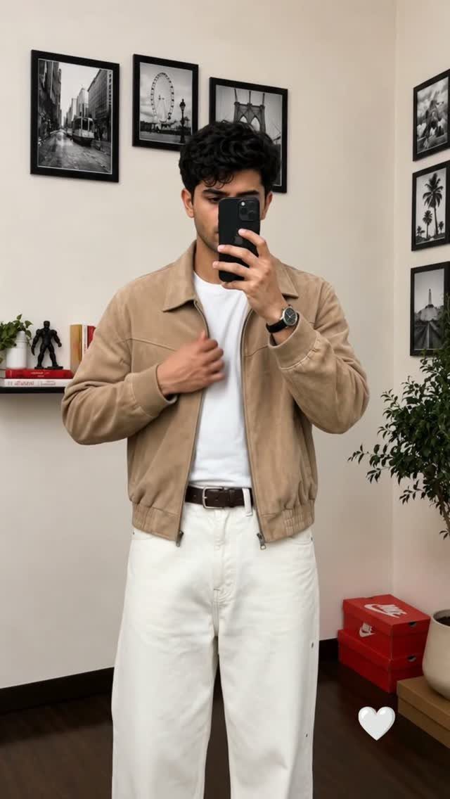 Man wearing a tan suede jacket, white t-shirt, and white jeans posing for a selfie.