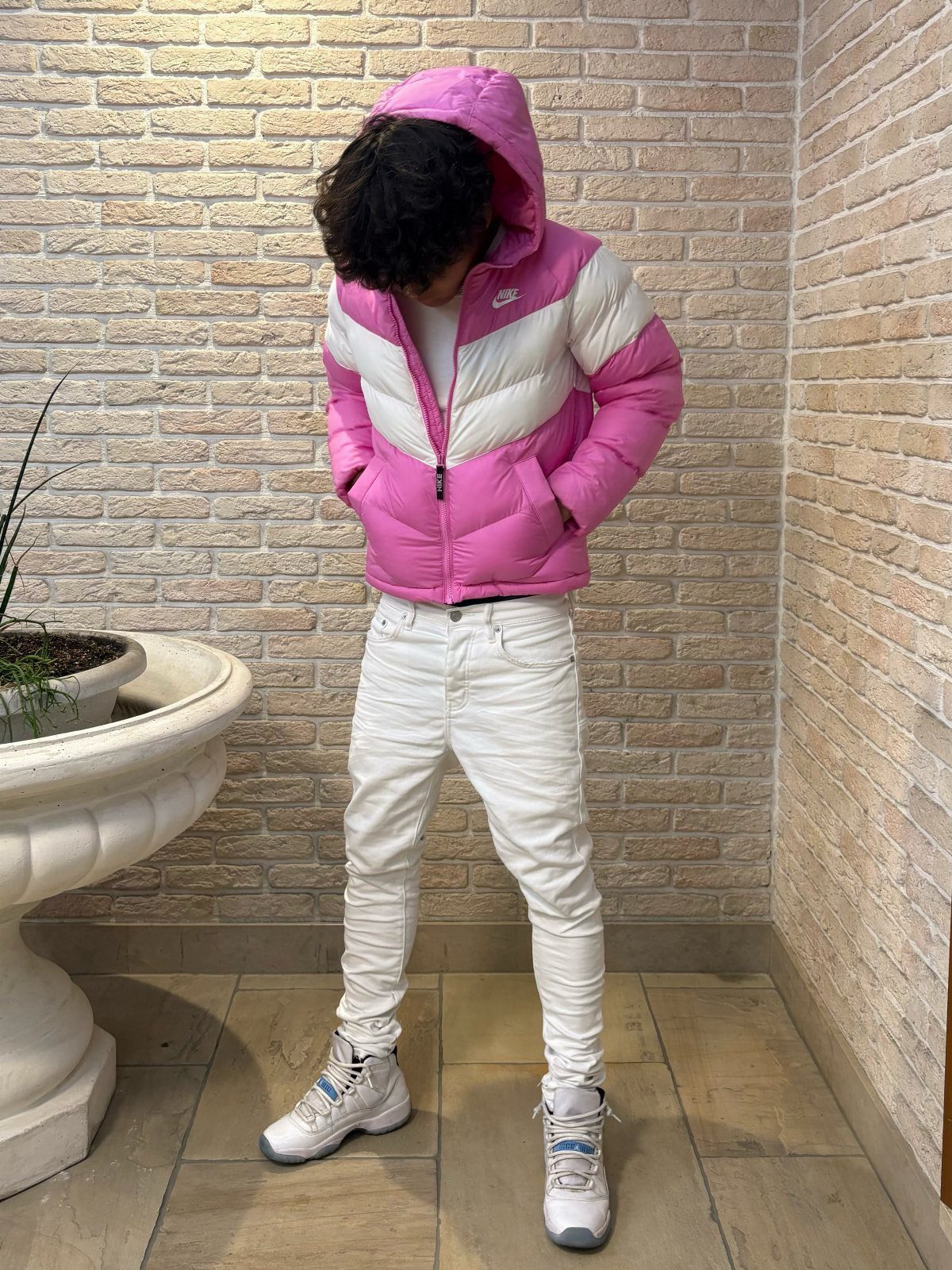 Person wearing a pink and white puffer jacket with white jeans and sneakers.