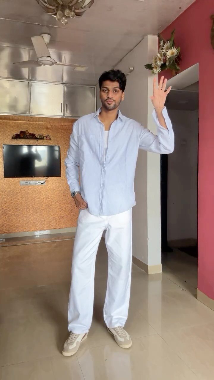 Man posing in a light blue shirt and wide-leg white pants with beige sneakers.