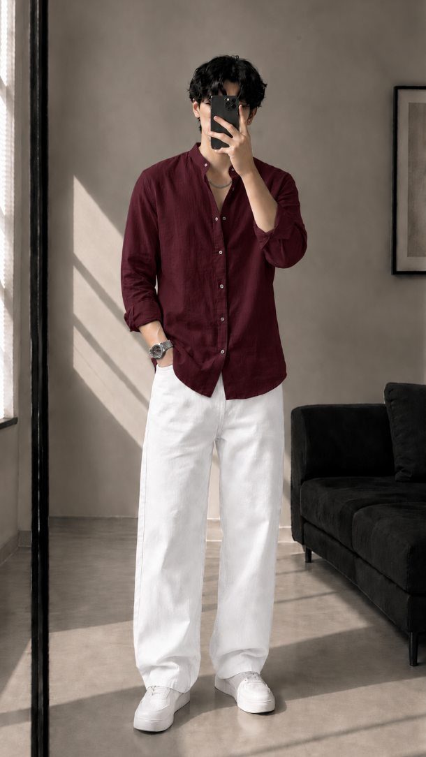 A person posing in a maroon shirt and wide white pants while taking a selfie.