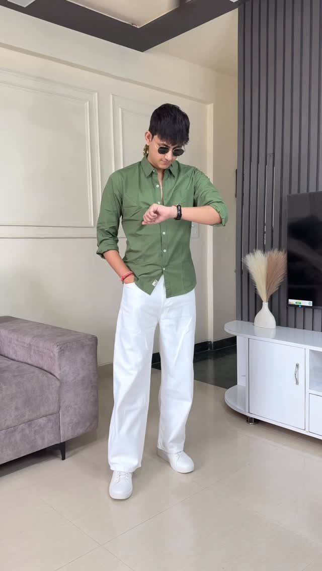 Man posing in an olive green shirt and wide-leg white pants with white sneakers.